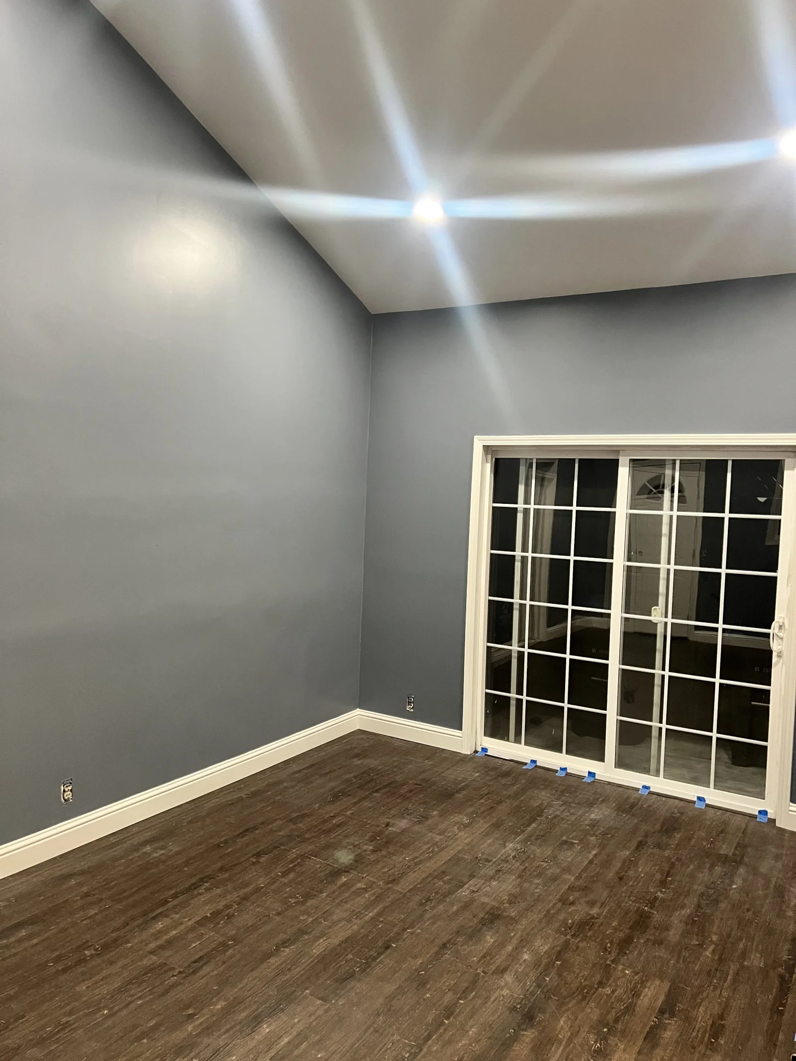 Empty room with slate-gray painted walls, white baseboards, dark wood-look vinyl plank flooring, and white grid sliding glass doors