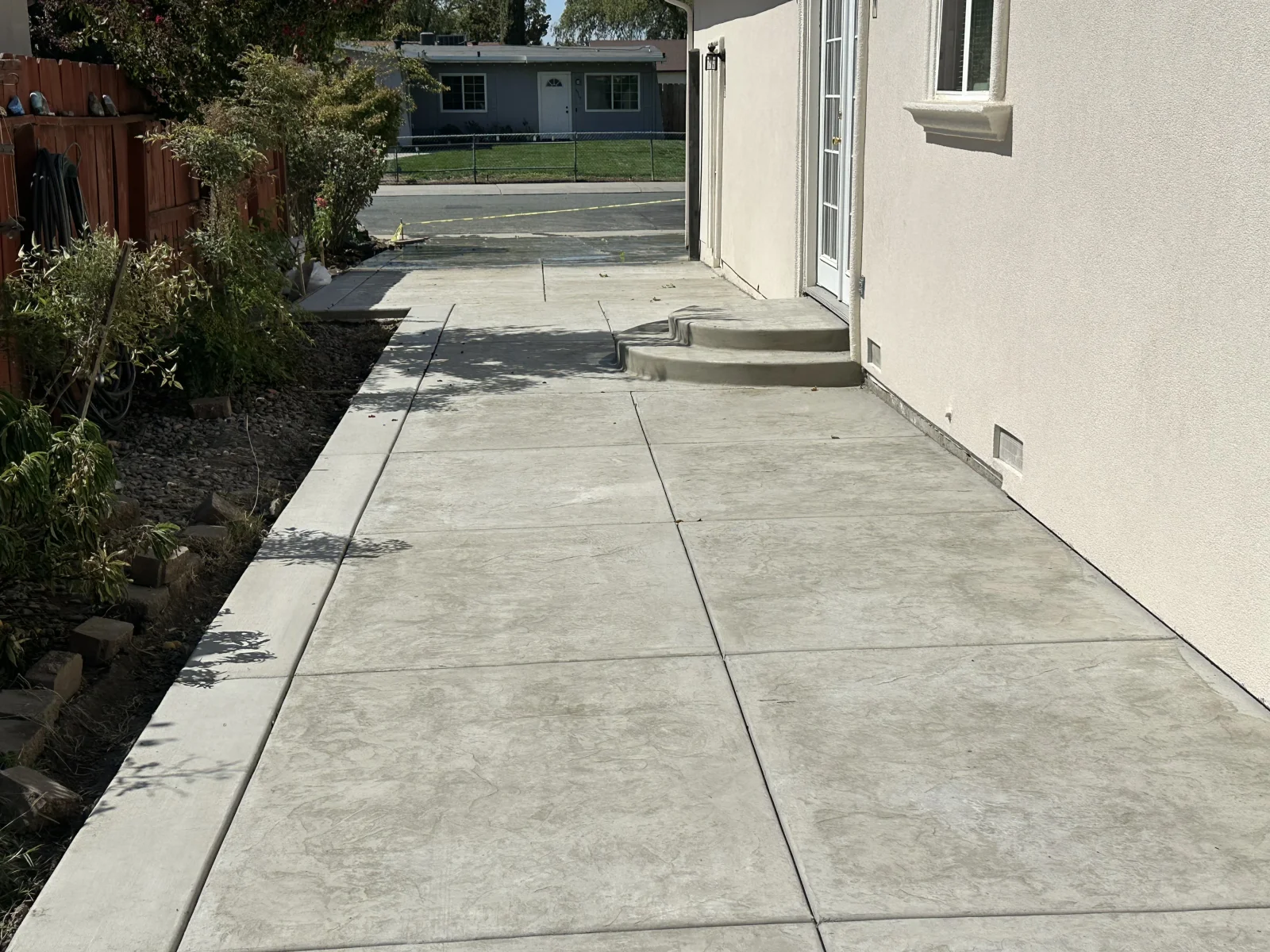 Stamped concrete side walkway with curved entry steps, saw-cut control joints, and raised concrete curb beside a stucco wall