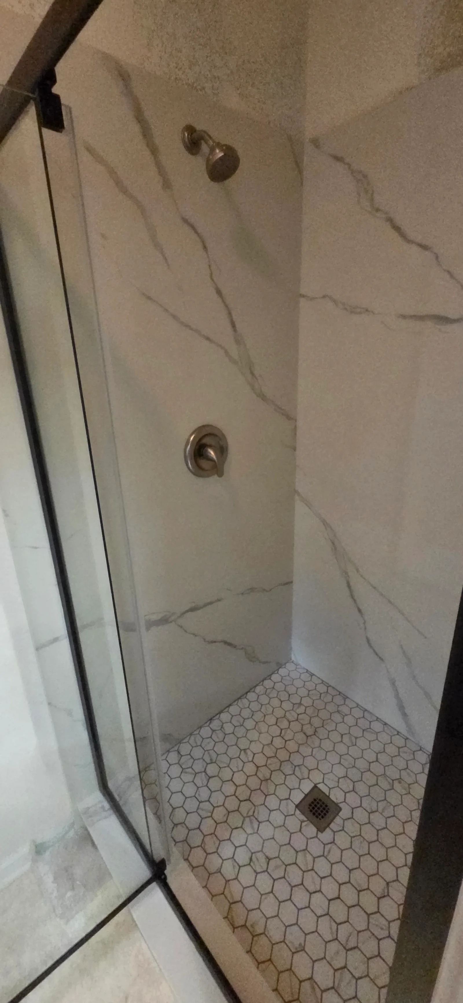 Walk-in shower with marble-look wall tile, white hex mosaic floor, brushed nickel fixtures, and frameless glass enclosure