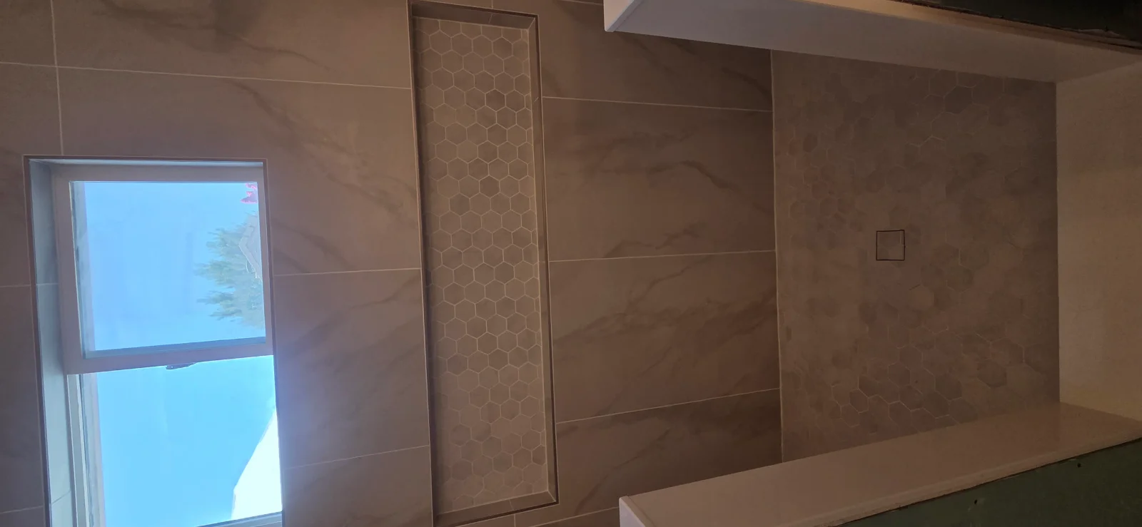 Shower wall with large marble-look porcelain tile, hexagon mosaic recessed niche, and hex-tiled valve wall