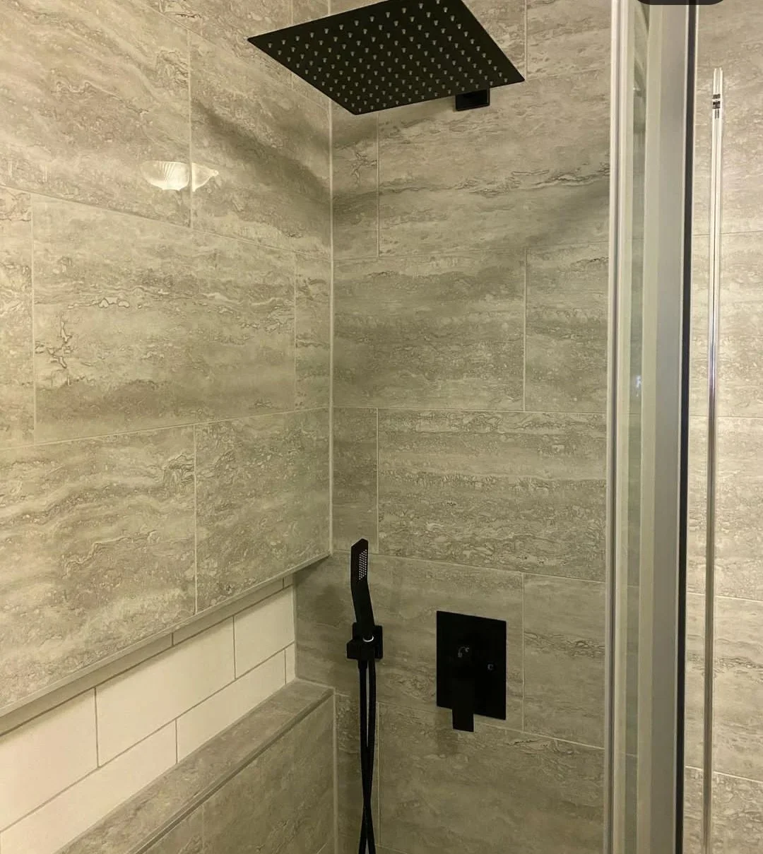 Gray travertine-look porcelain tile shower with matte black rain showerhead, handheld wand, and square valve trim