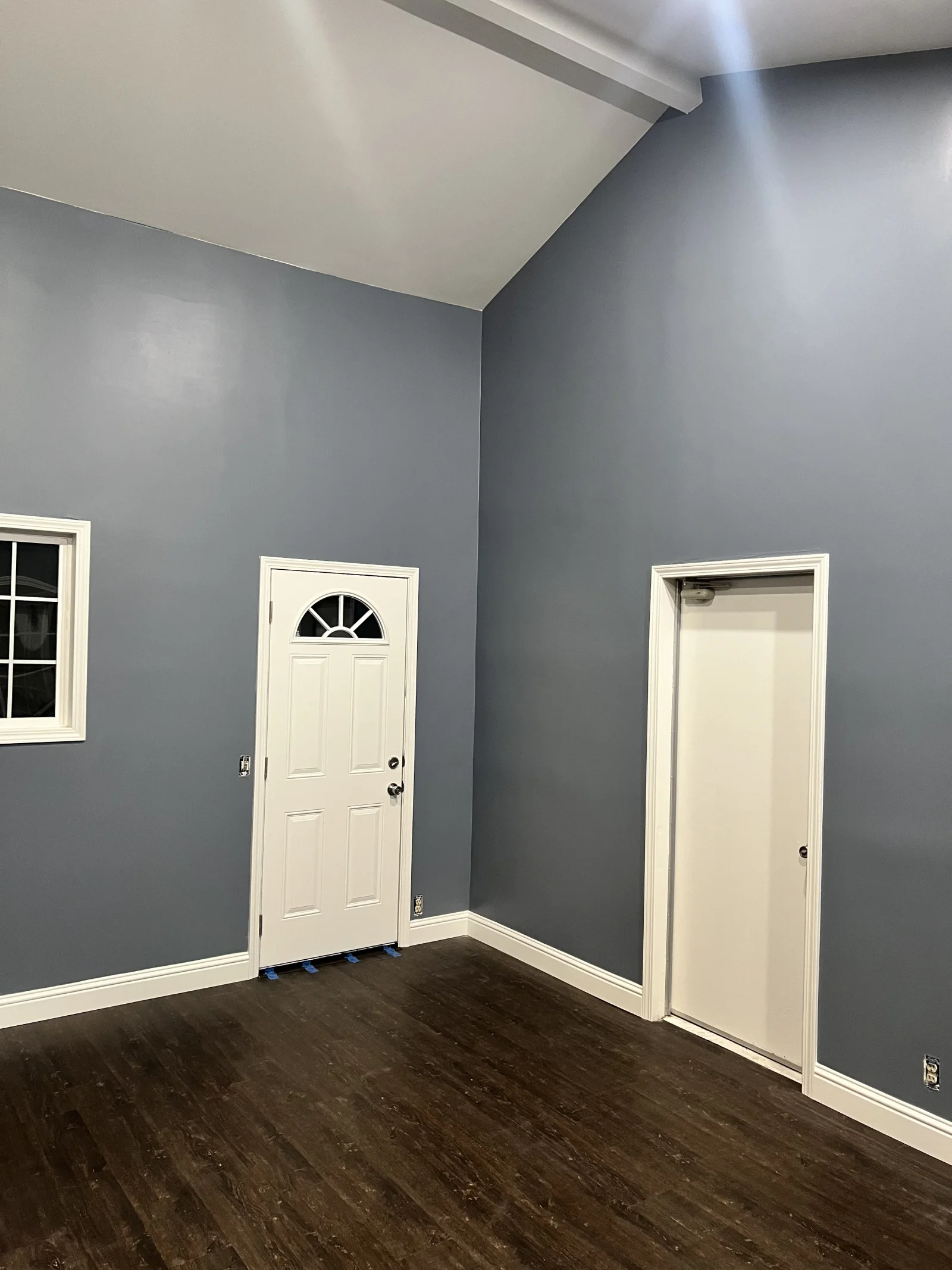 Vaulted room with slate blue-gray painted walls, white beam and trim, white six-panel door, and dark wood-look vinyl plank flooring