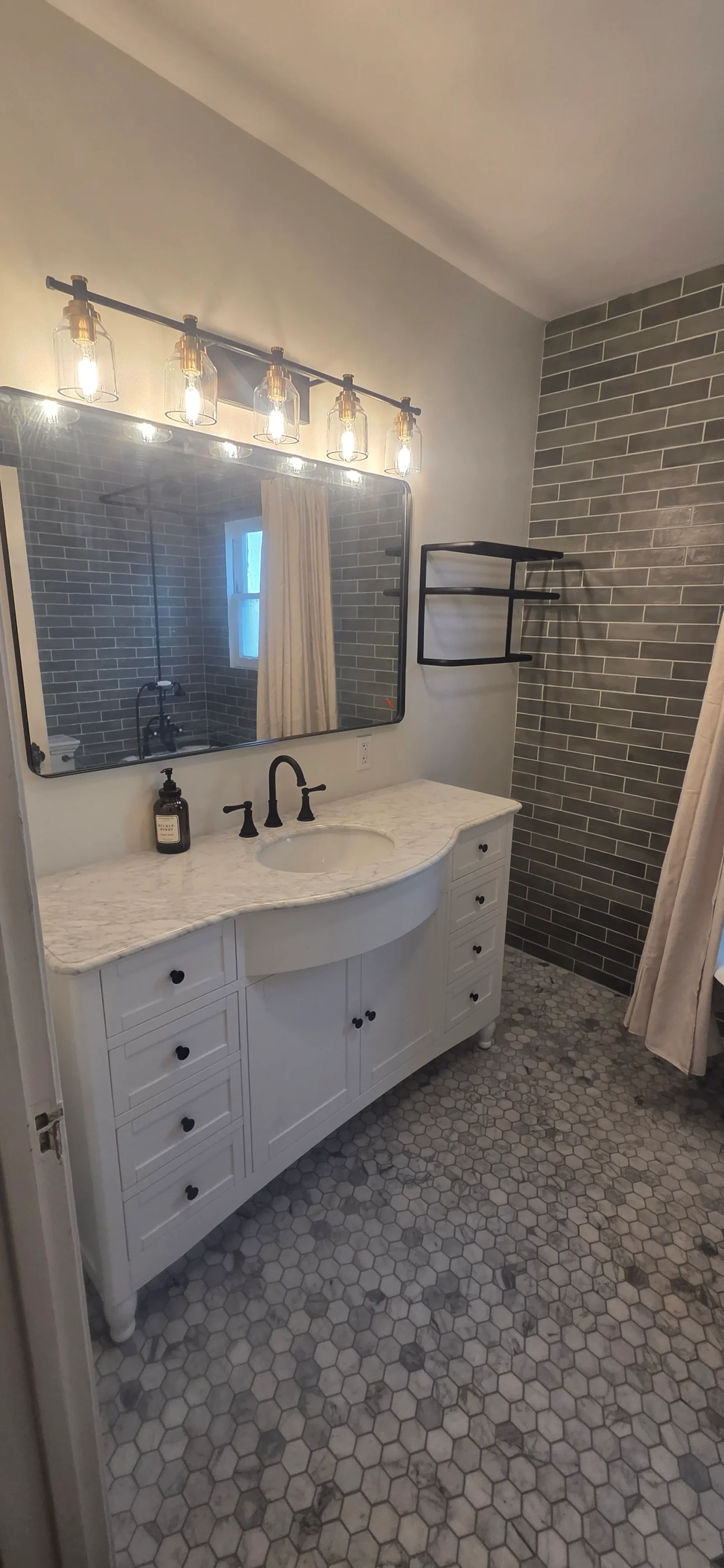 White vanity with marble countertop, matte black faucet, hex mosaic floor, and gray subway tile wall
