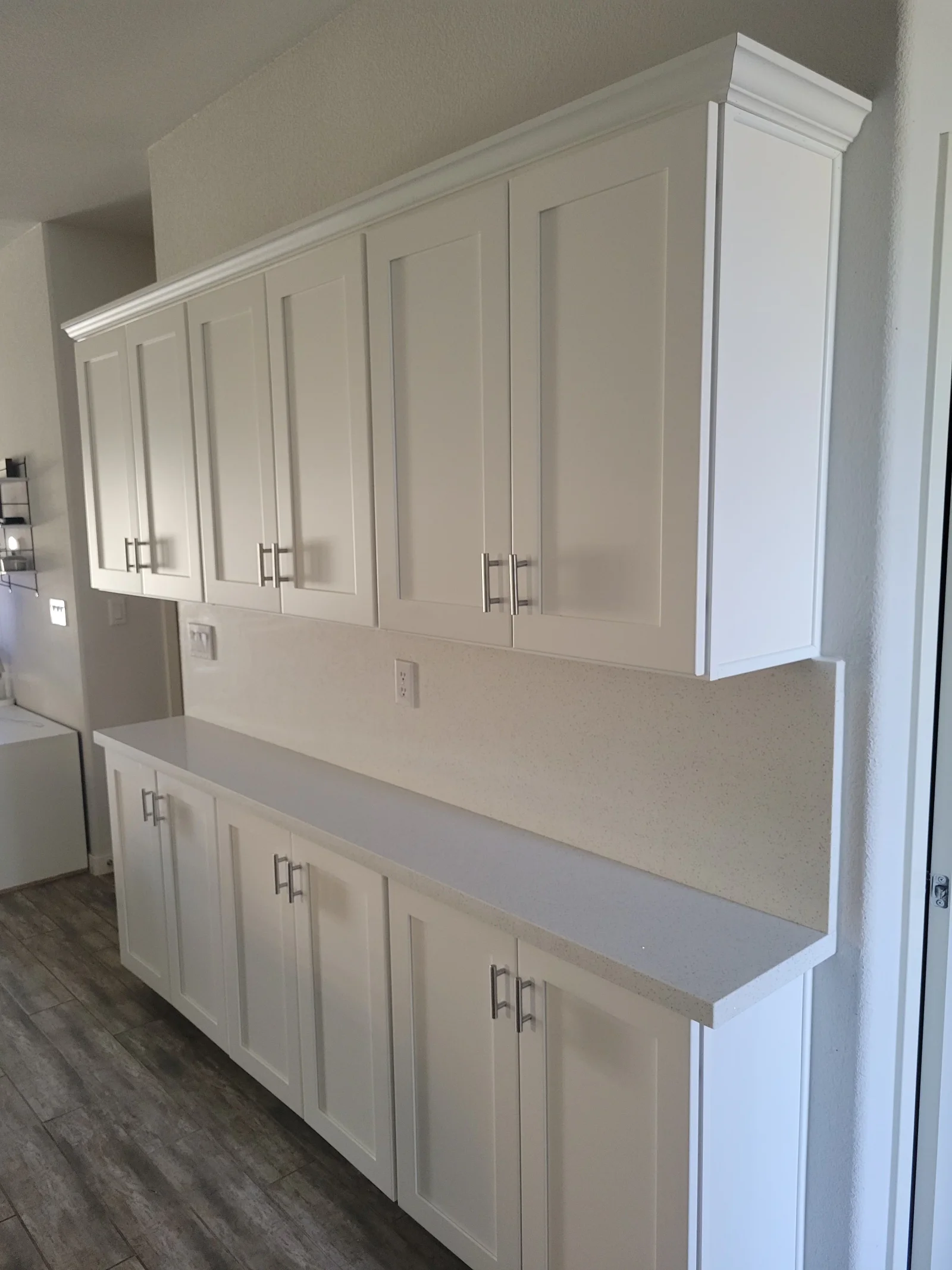 White shaker upper and base cabinets with brushed nickel bar pulls, crown molding, and light gray speckled quartz countertop